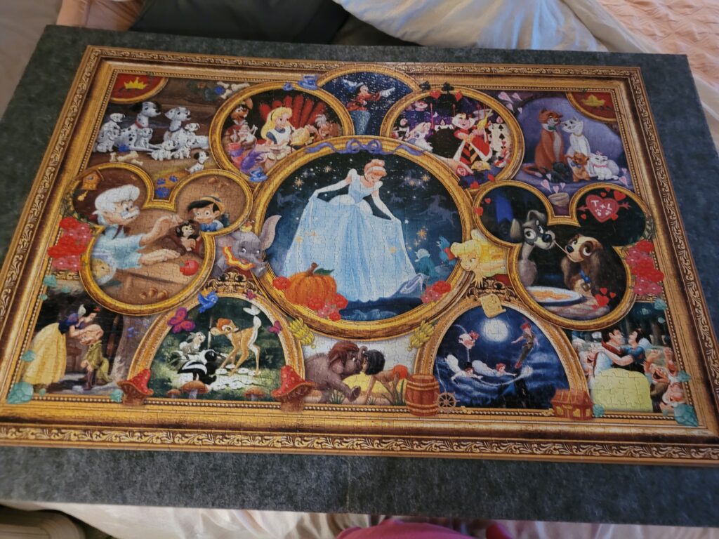 A puzzle board with a completed 2000 piece Ceaco Disney puzzle, showcasing the satisfying result of puzzling as a hobby.